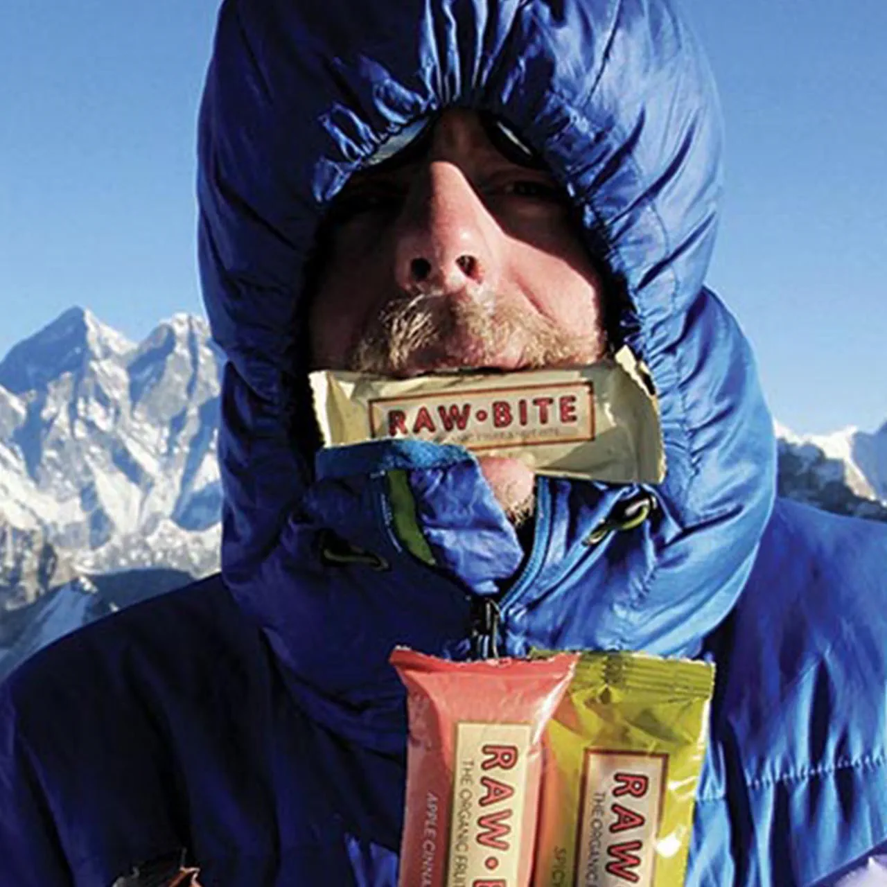 A person bundled in a blue insulated jacket, holding multiple Rawbite snack bars.